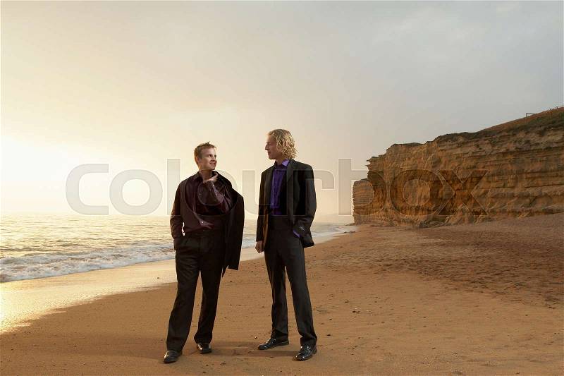 Two men standing on beach at sunset, stock photo
