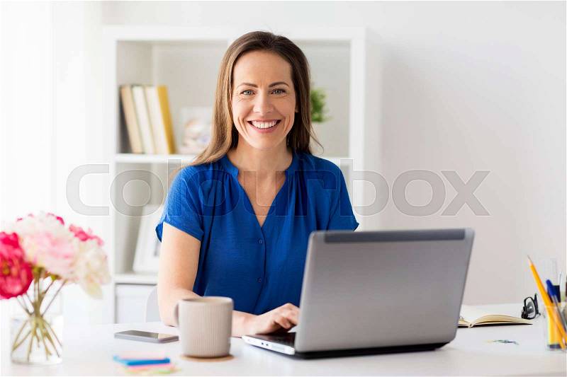 Business, people and technology concept - happy smiling woman with laptop computer working at home or office, stock photo