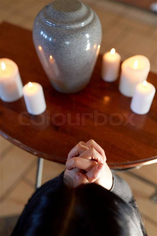 Cremation, people and mourning concept - sad woman with cinerary urn and candles praying at funeral in church, stock photo