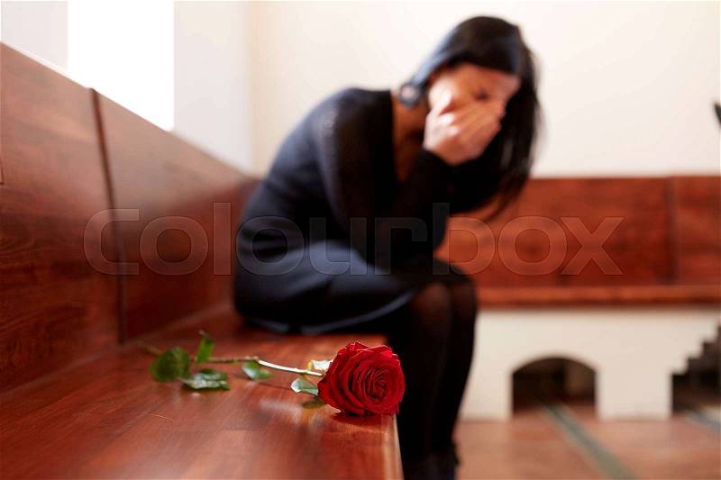 People, grief and mourning concept - crying woman with red rose sitting on bench at funeral in church, stock photo