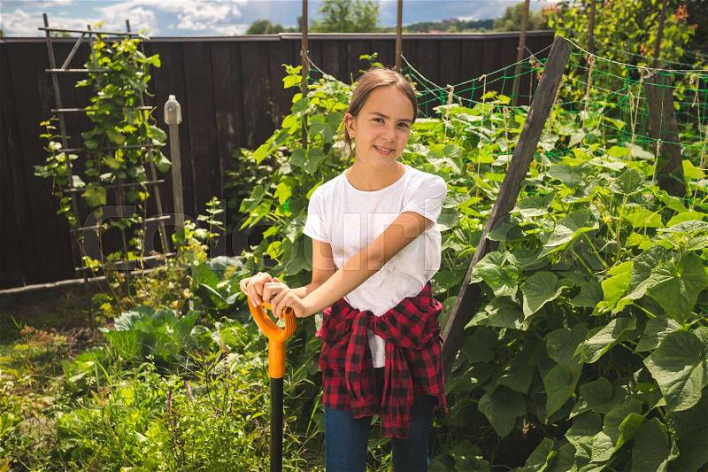 Young girl in wellington boots holding shovel and working at garden, stock photo