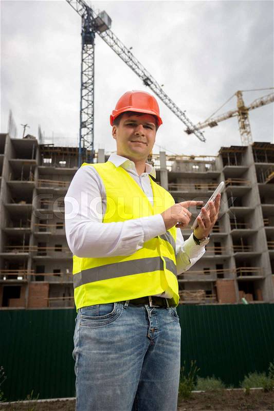 Smiling engineer using digital tablet at building site, stock photo