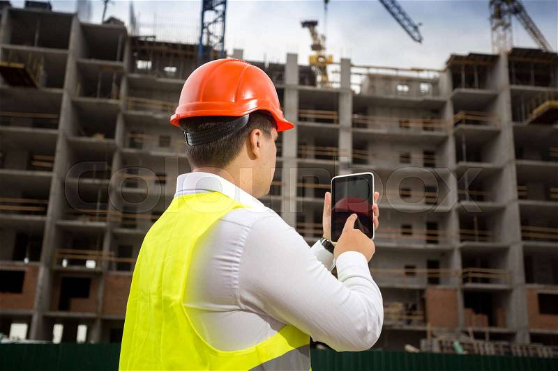 Rear view of building inspector holding digital tablet and inspecting building under construction, stock photo