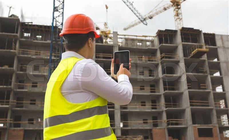 Young engineer in hardhat on building site with digital tablet, stock photo