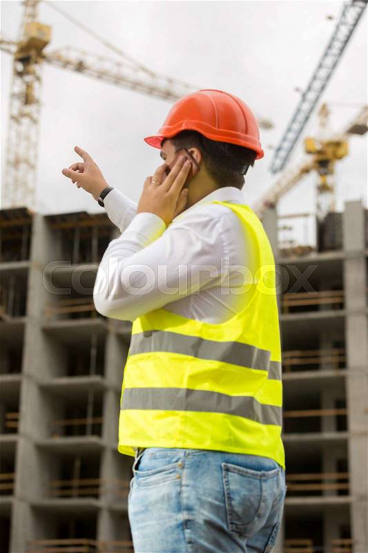 Construction engineer pointing with finger at building under construction, stock photo