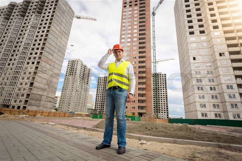 Businessman in hardhat and safety vest standing on building site, stock photo