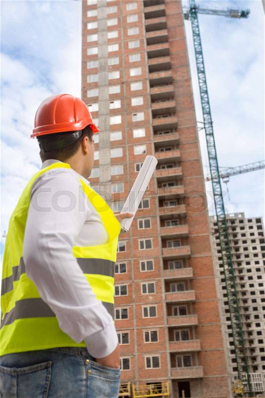 Building inspector pointing at building under construction, stock photo