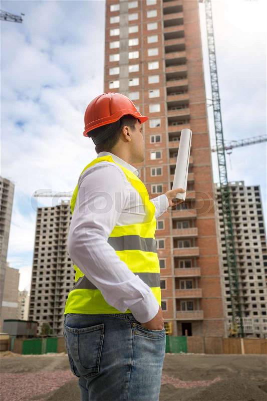 Construction engineer pointing at building under construction, stock photo
