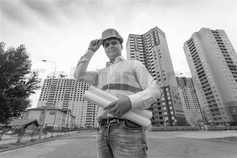 Black and white portrait of young smiling engineer standing at building site, stock photo