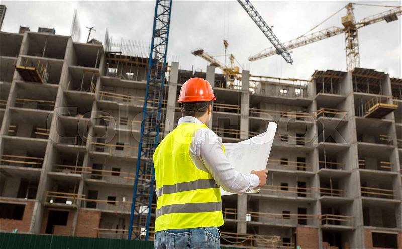 Architect in hardhat pointing at building under construction, stock photo
