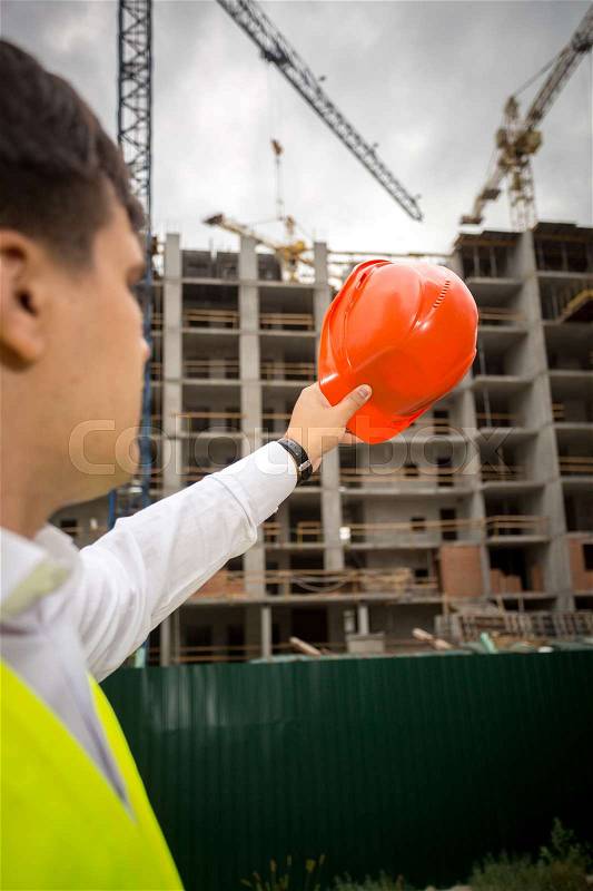 Construction engineer pointing at building site with red hardhat, stock photo