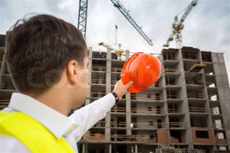 Rear view shot of engineer pointing at building site with red hardhat, stock photo