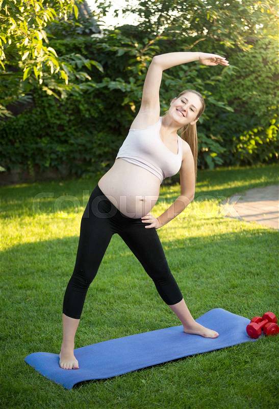 Beautiful young pregnant woman exercising on green grass at park, stock photo