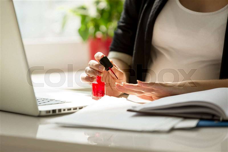 Closeup image of businesswoman painting fingernails at work, stock photo