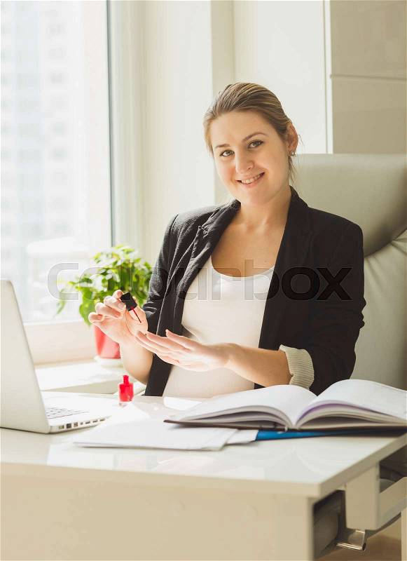 Portrait of beautiful smiling secretary painting nails at office, stock photo