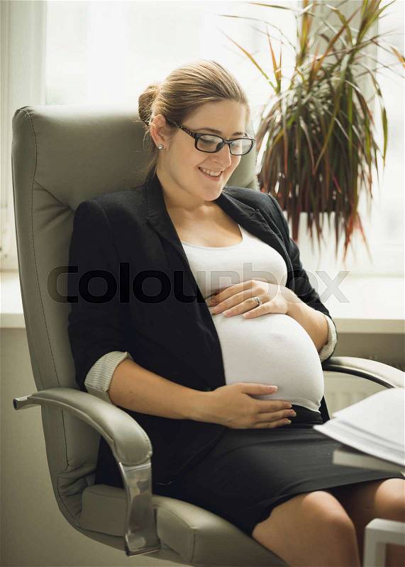 Portrait of beautiful pregnant businesswoman touching big belly, stock photo