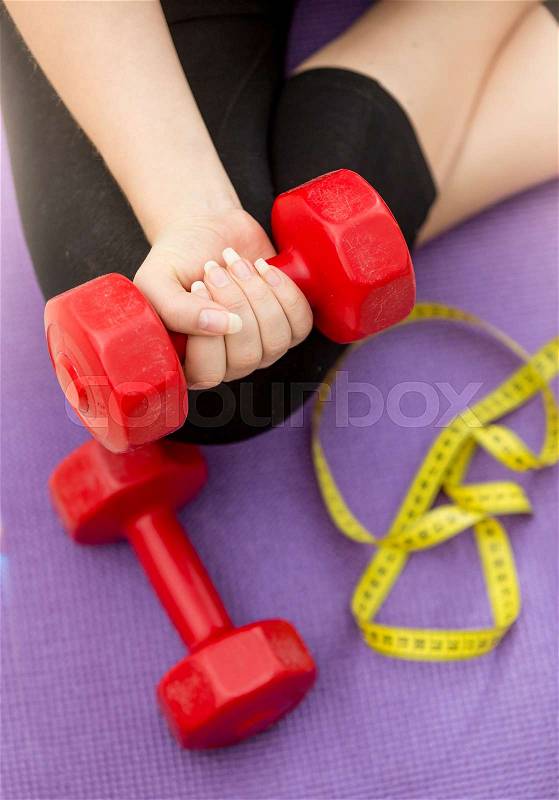 Closeup photo of female hand lifting dumbbell from fitness mat next to measuring tape. Concept of fitness and losing weight, stock photo
