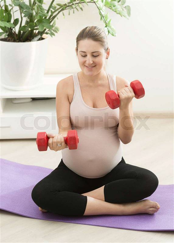 Pregnant woman exercising with dumbbells at home, stock photo