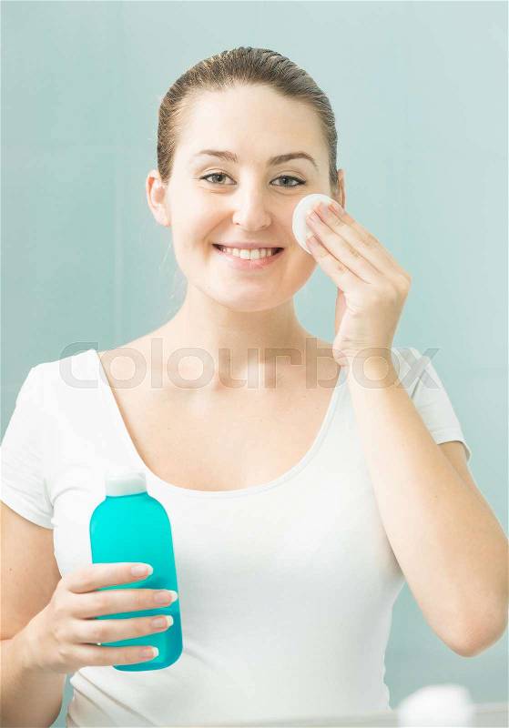 Portrait of beautiful smiling woman cleaning face with lotion, stock photo