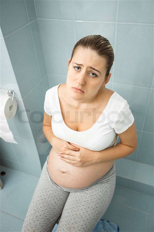 Portrait of upset pregnant woman feeling unwell using toilet, stock photo