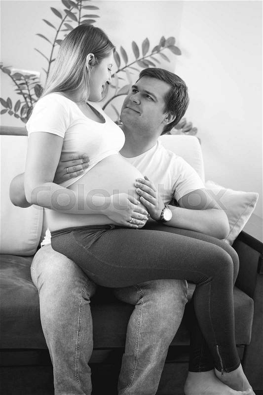 Black and white image of happy young pregnant couple smiling and looking on big belly, stock photo