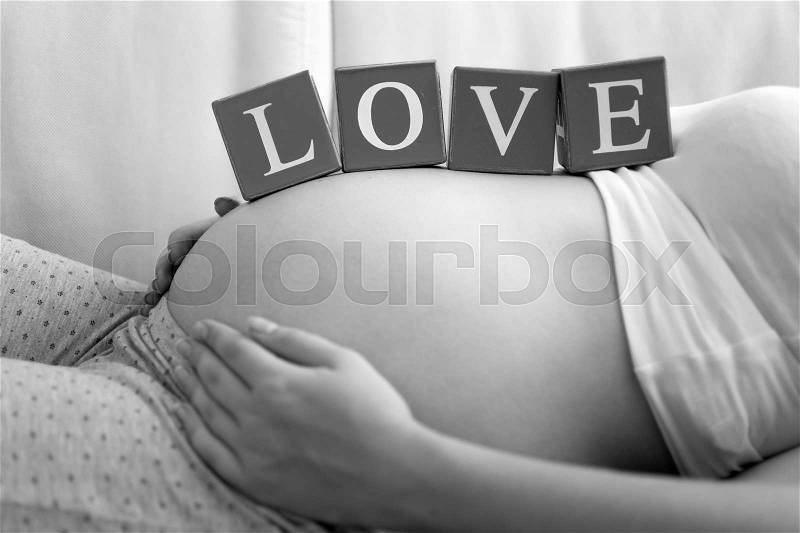 Black and white image of young pregnant woman with word Love on tummy, stock photo