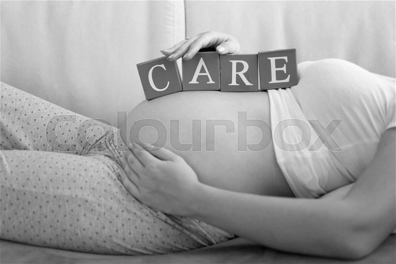 Black and white image of letters on wooden blocks making word Care on pregnant women tummy, stock photo