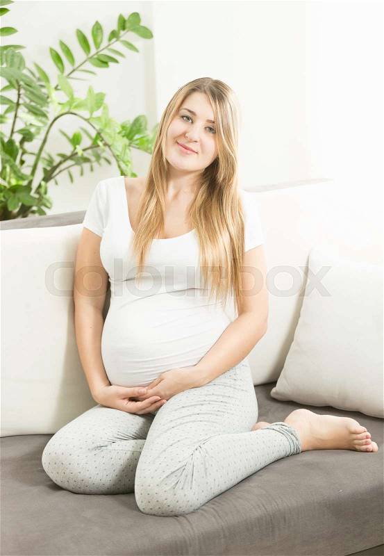 Beautiful smiling expectant mother sitting on sofa at living room, stock photo
