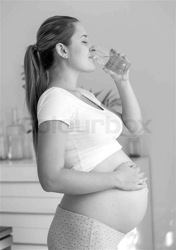 Black and white portrait of beautiful pregnant woman drinking water at living room, stock photo