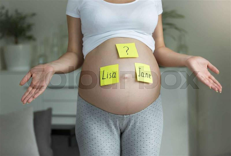 Concept of choosing baby\'s name.Young regnant woman with names written on belly, stock photo