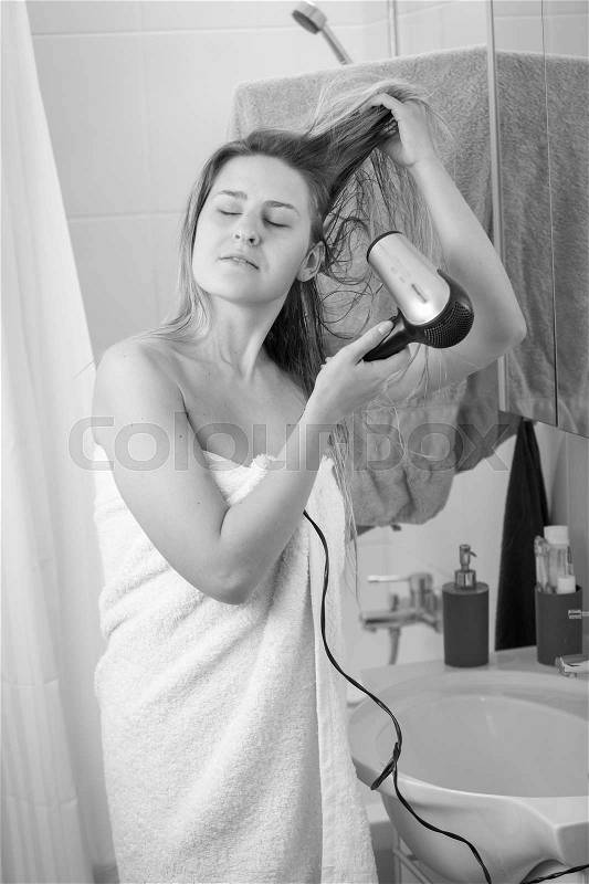 Black and white image of young woman in with hairdryer at bathroom mirror, stock photo
