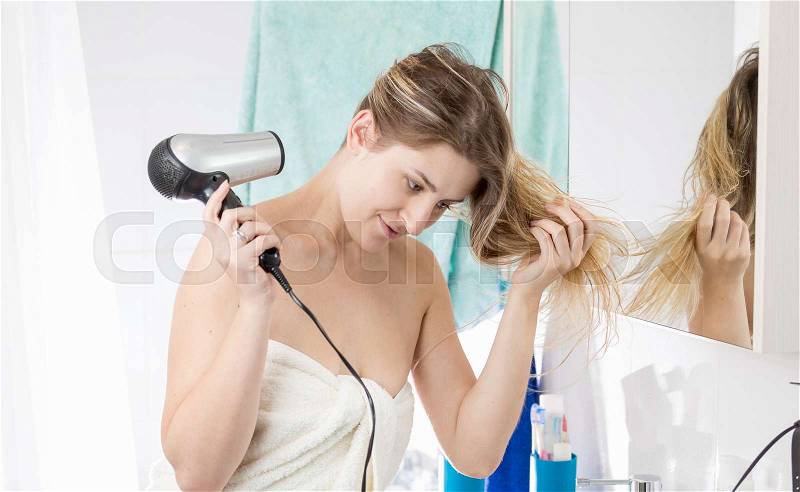 Woman drying hair with hairdryer after having bath, stock photo