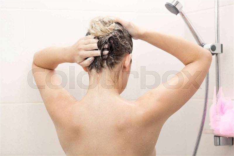 Sexy brunette woman washing hair with shampoo at shower, stock photo