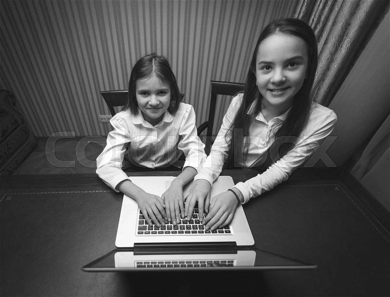 Black and white portrait of two teen girls using laptop at cabinet, stock photo