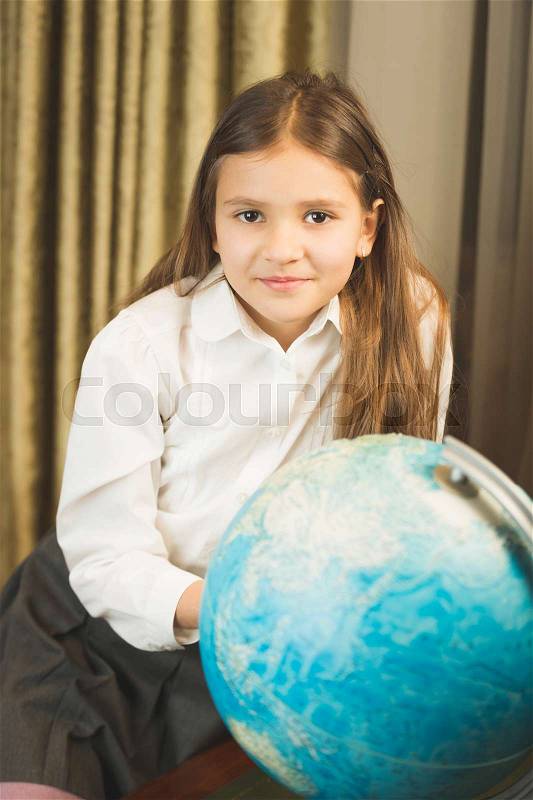 Portrait of smiling schoolgirl posing with Earth globe at cabinet, stock photo