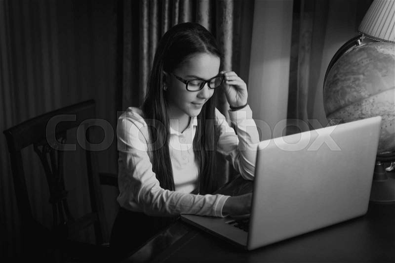 Black and white image of beautiful schoolgirl wearing eyeglasses posing with laptop, stock photo