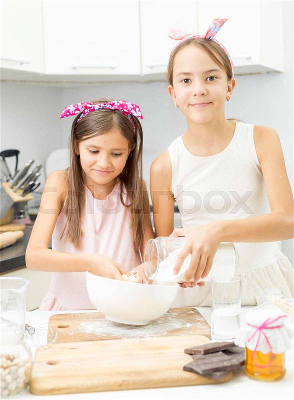 Two sisters making dough on kitchen in big white bowl, stock photo
