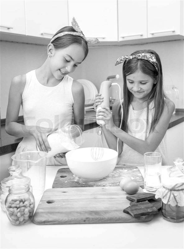 Black and white portrait of two smiling girls cooking pie and making dough, stock photo