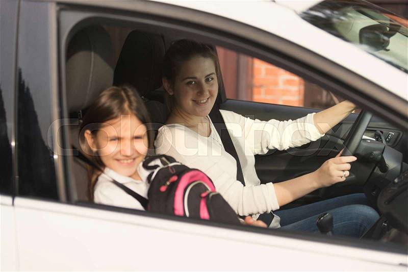Beautiful mother driving car with daughter to school, stock photo