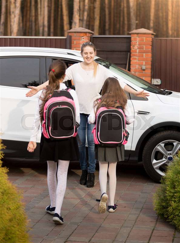Happy young mother meeting her two daughters after school at car, stock photo