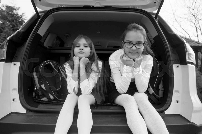 Black and white photo of two smiling schoolgirls sitting in open car trunk, stock photo