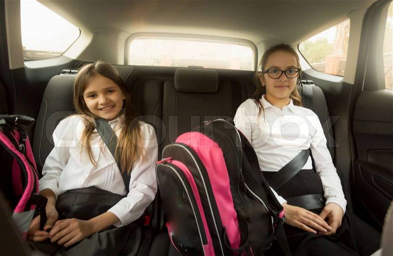 Two cheerful schoolgirls sitting on car back seat, stock photo