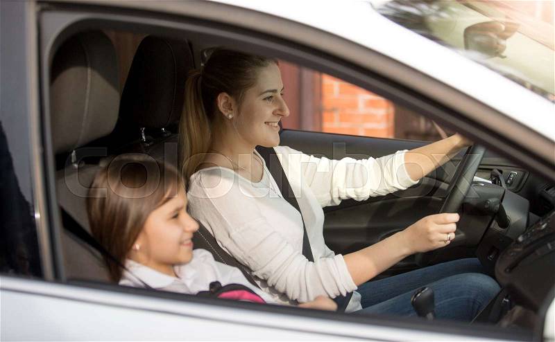 Young mother driving car to school with daughter, stock photo