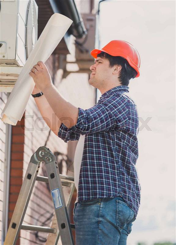 Engineer in hardhat looking in plan of air conditioning system, stock photo