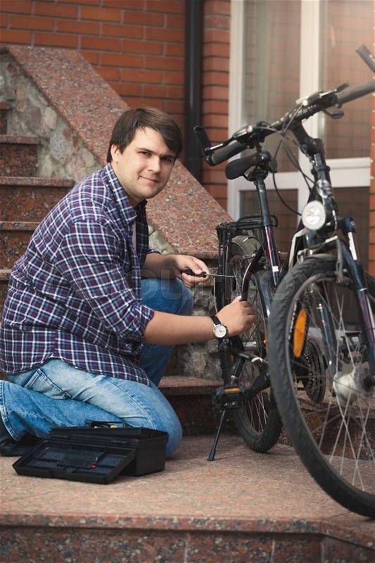 Young man repairing bicycle on porch of house, stock photo