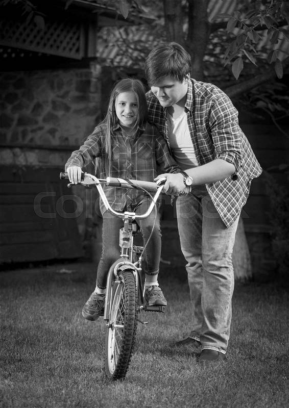 Monochrome image of happy father teaching his daughter how to ride a bicycle, stock photo