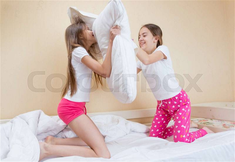 Two sisters in pajamas fighting with pillows on bed, stock photo