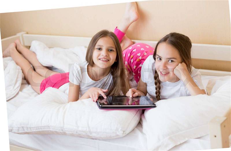 Two cheerful teenage girls lying on bed and using digital tablet, stock photo