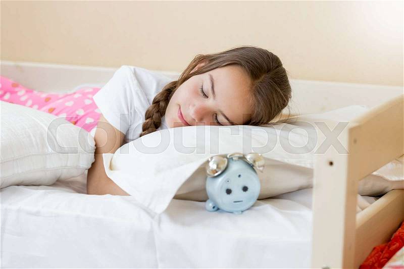 Young woman holding hand on alarm clock and turning it off, stock photo