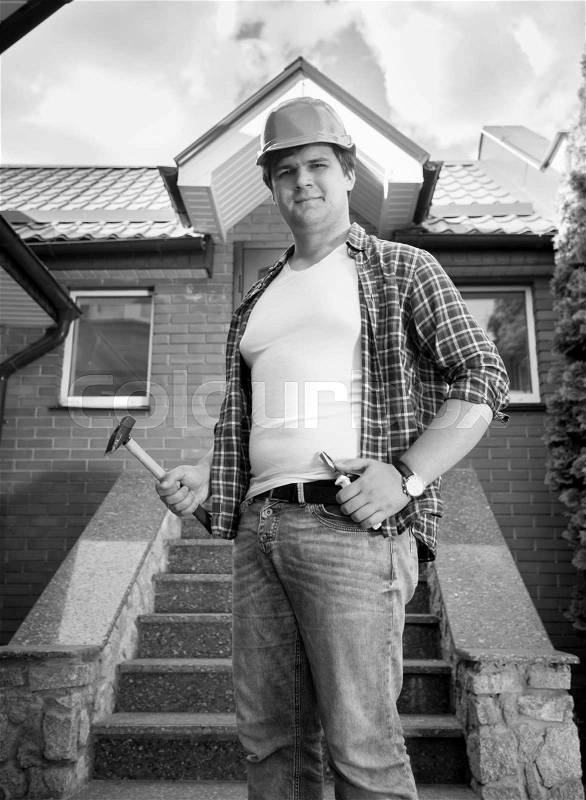 Black and white portrait of smiling construction worker posing in front of finished house, stock photo
